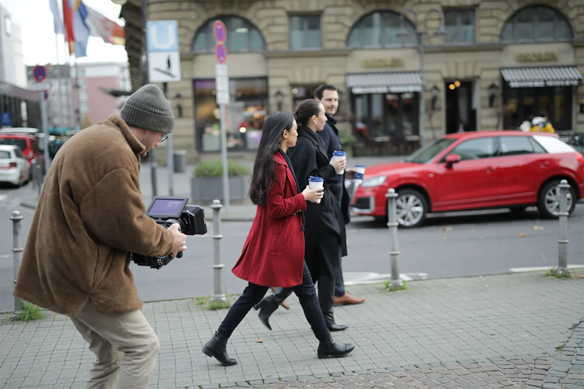 BTS of lawyers walking down a street being filmed with cameras.